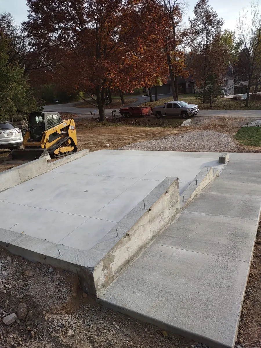 Concrete slab with a poured ramp and a skid steer behind it