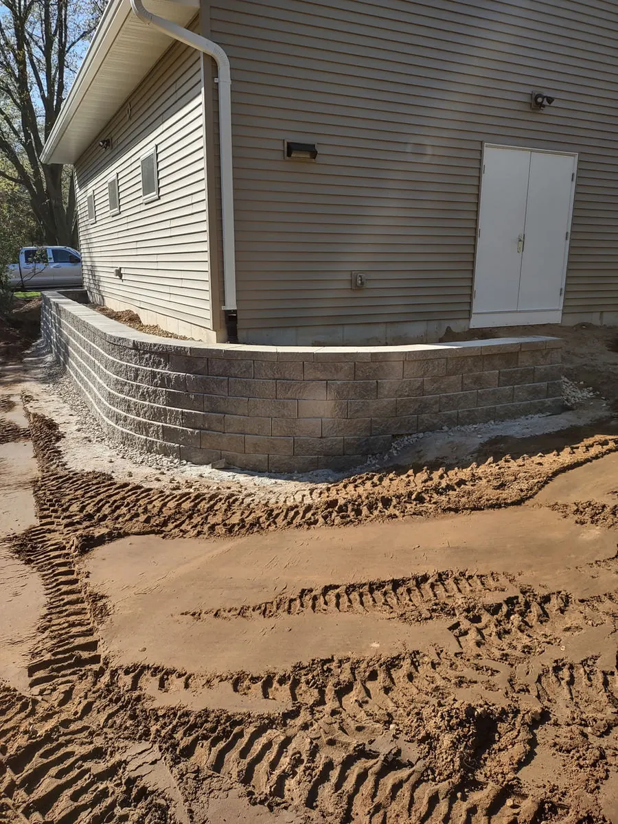 Block retaining wall wrapping the corner of a building on graded soil